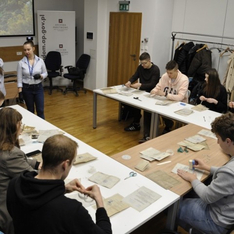 Powiększ obraz: studzenci siedzą przy stołach w sali konferencyjnej, na stołach materiały do konserwacji akt