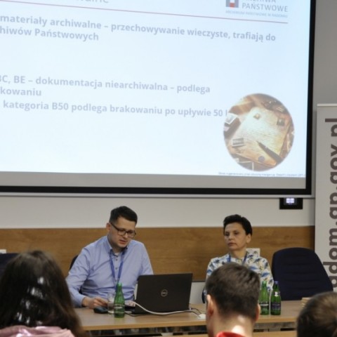 Powiększ obraz: w tle prezentacja dla studentów, widok na prowadzących spotkanie